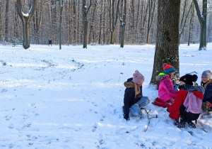 Cztery dziewczynki odpoczywają, siedząc na śniegu pod drzewem.